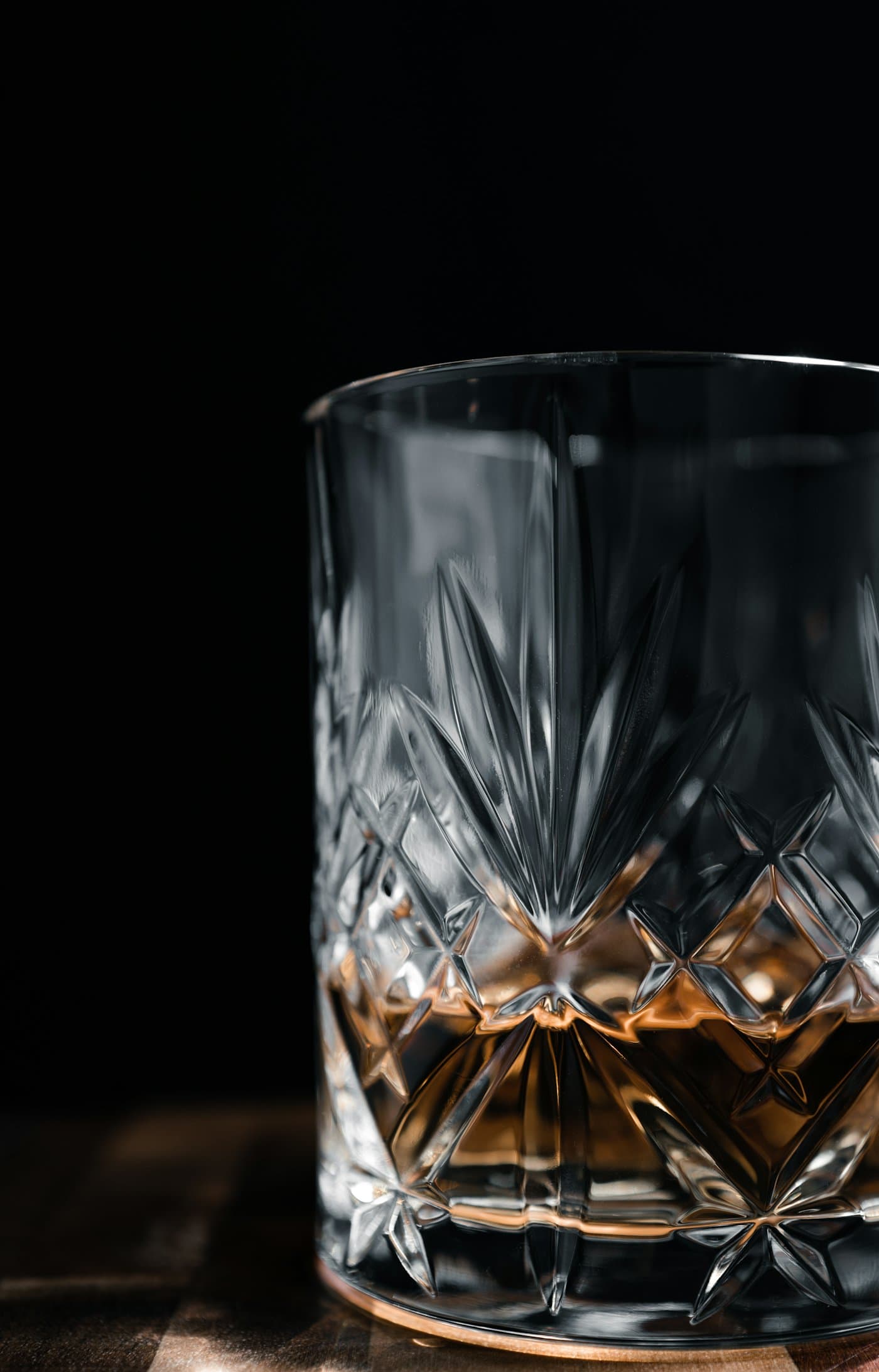 Cut-crystal tumbler holding a measure of whisky against a dark background