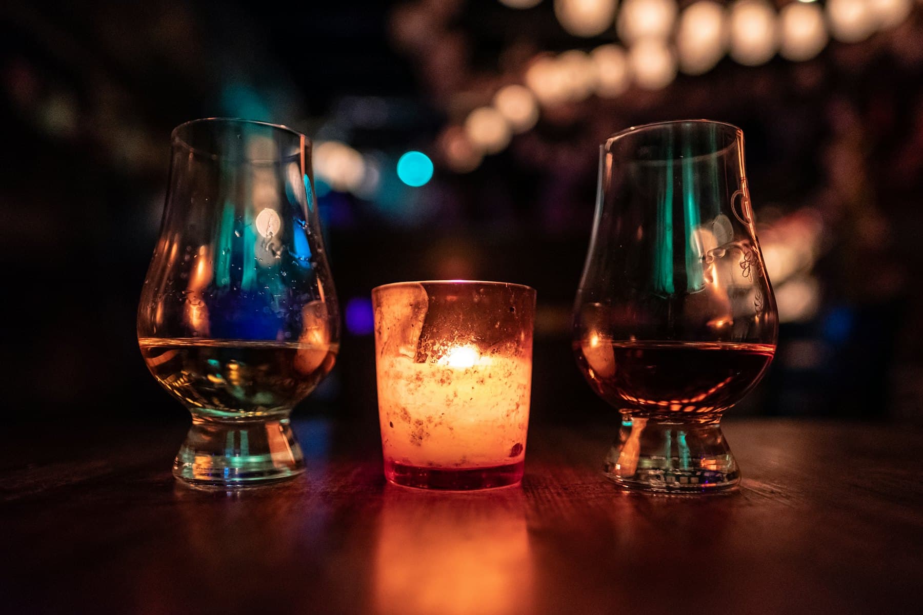Two whisky nosing glasses beside a candle in a dimly lit bar