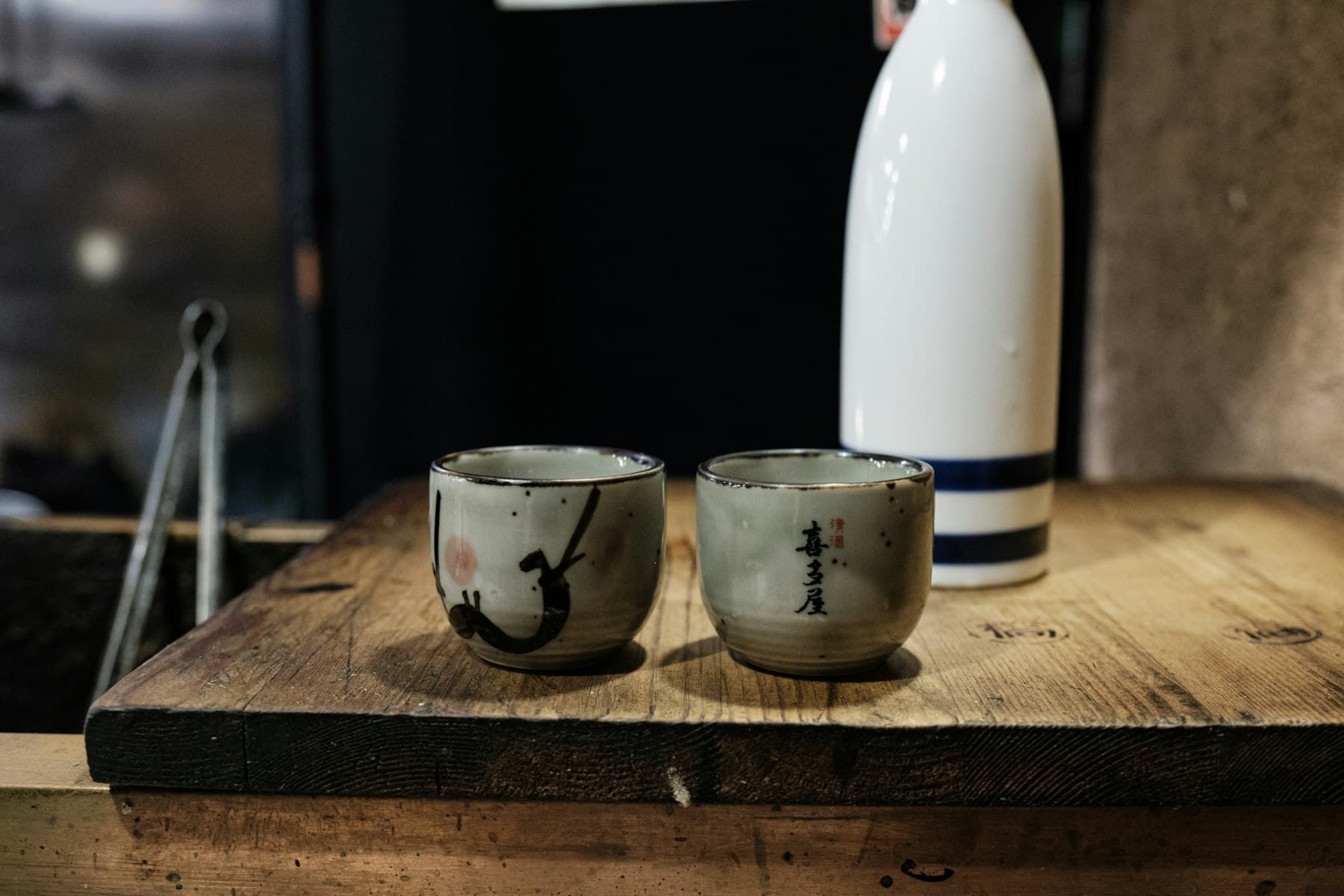 Two ceramic sake cups and a tokkuri flask on a wooden counter